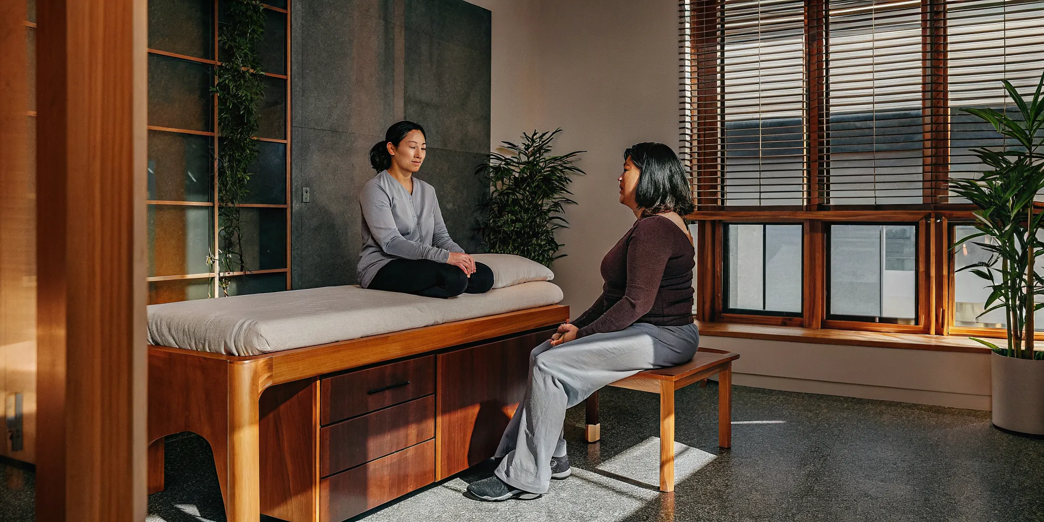 Female physical therapist sitting with a patient in a bright Brooklyn physical therapy treatment room