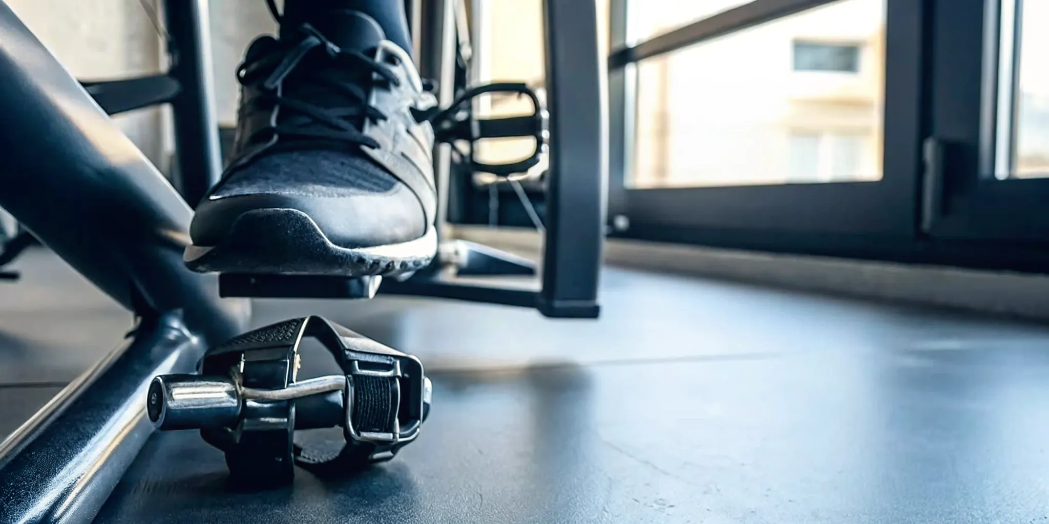 Indoor cycling shoe cleat beside athletic sneaker and bike pedal