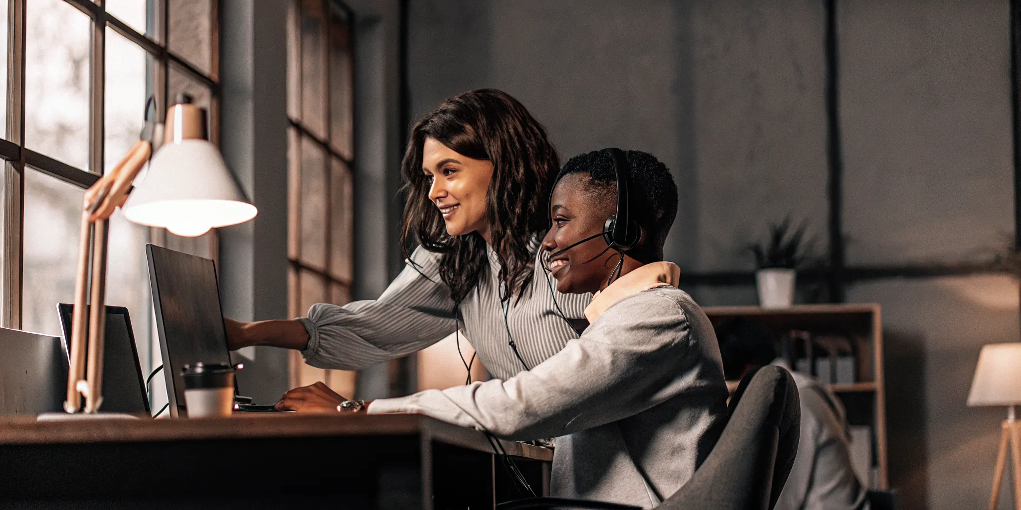Two contact center agents collaborating in a coaching session at their workspace