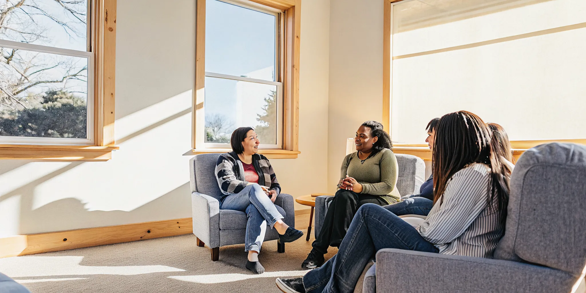 A supportive recovery group talking together in a warm circle in a bright community room