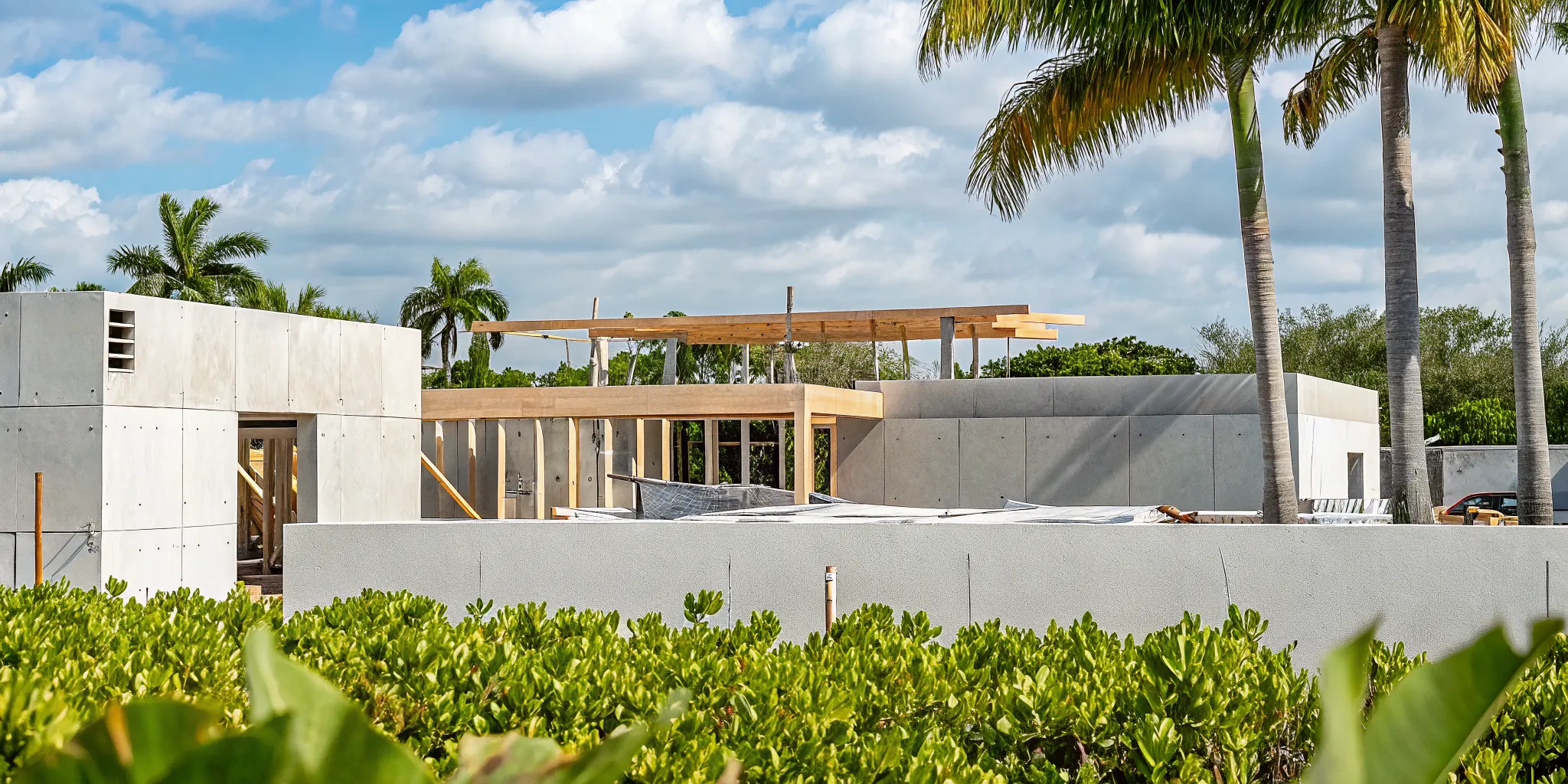 A modern Florida home construction site with wood framing and palm trees under a sunny blue sky