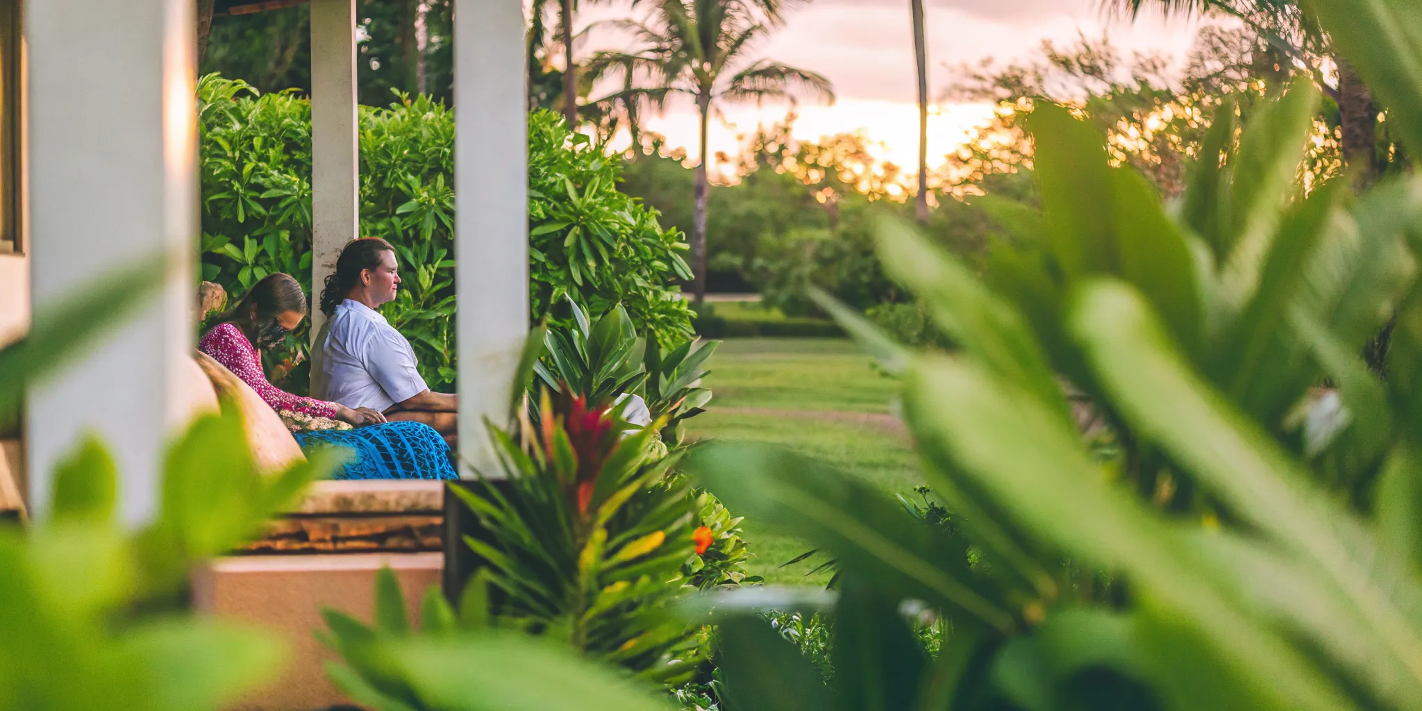 Peaceful outdoor group therapy setting on a Hawaiian lanai with tropical plants and warm sunset light