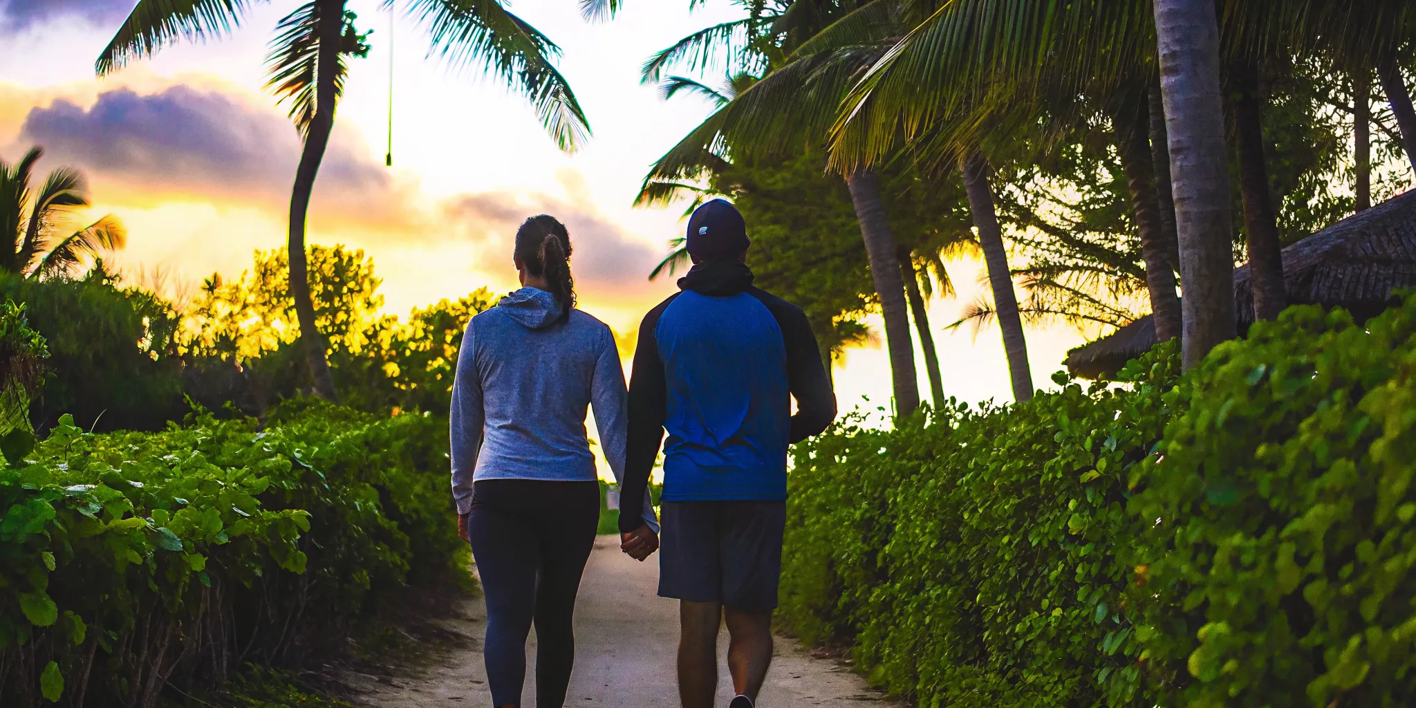 Two people walking together on a beach path at sunset showing the role of exercise in addiction recovery