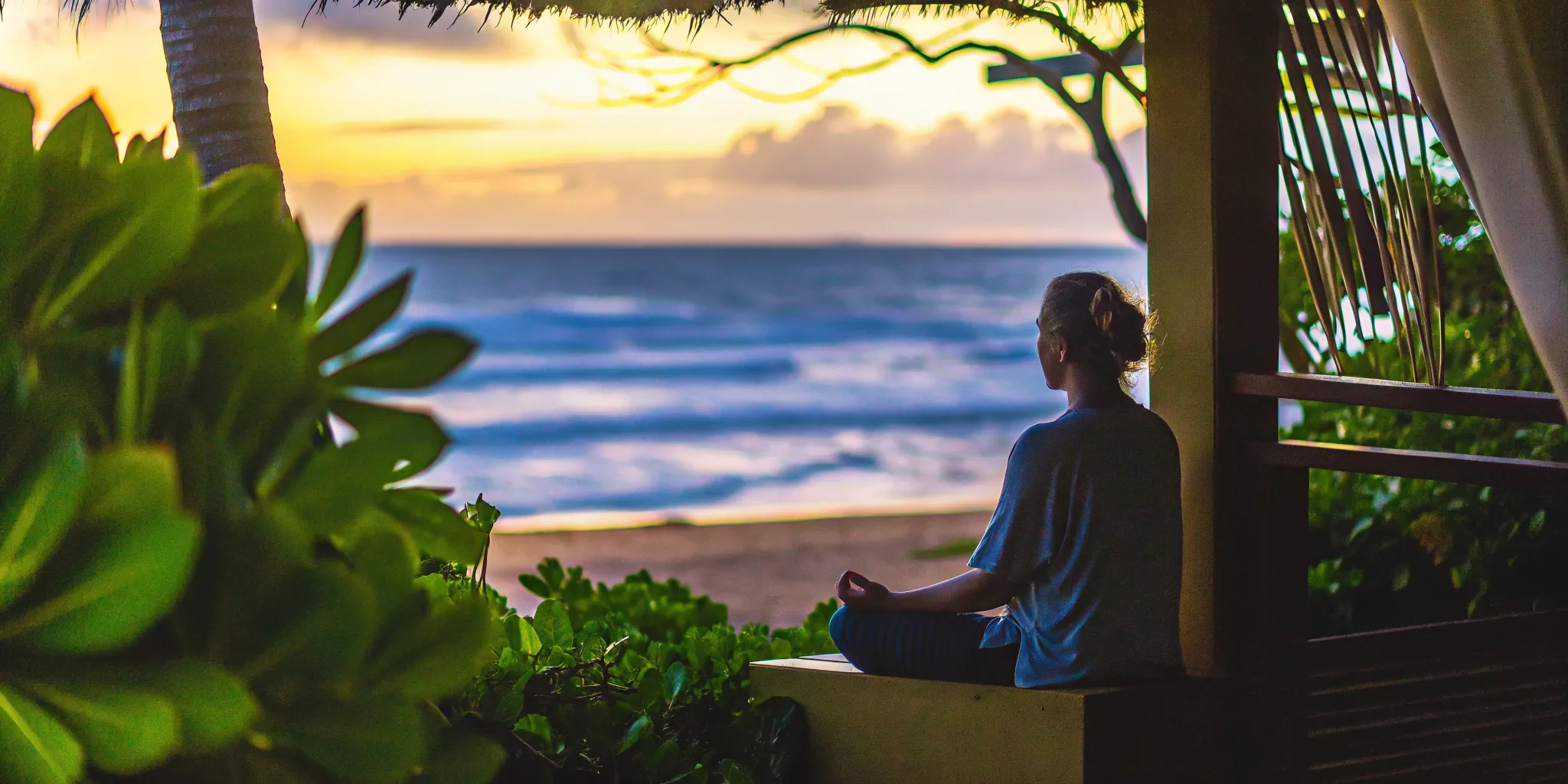 Person meditating on a Maui beach at sunset with gentle waves, representing peace and healing from trauma and addiction