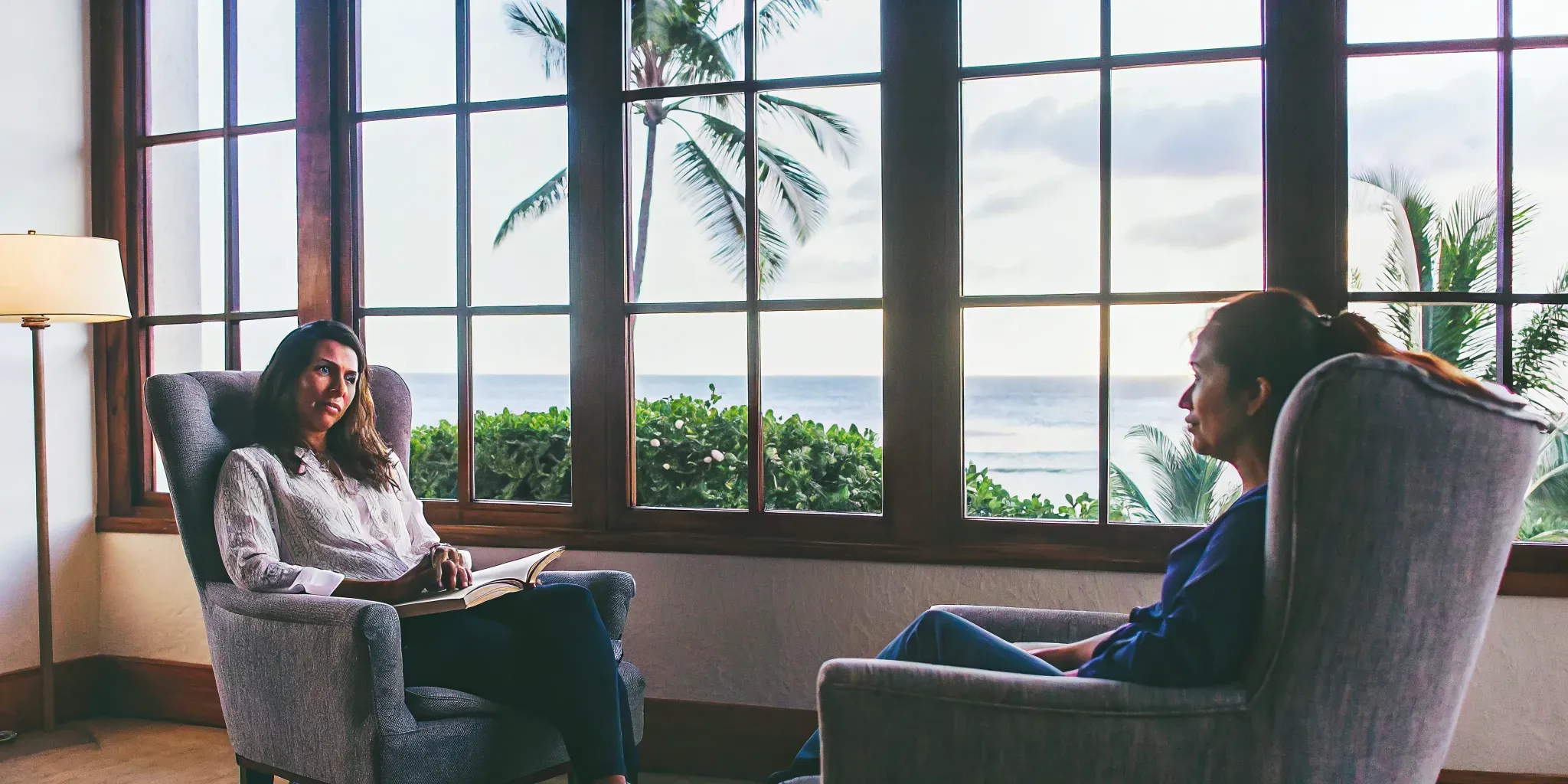 A therapist and client in a therapy session inside a modern Hawaii treatment center with large windows overlooking tropical greenery