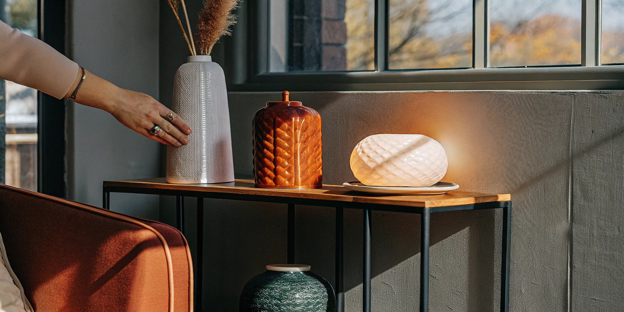 Warm light diffusing through a sculptural ceramic lamp shade beside a neutral sofa