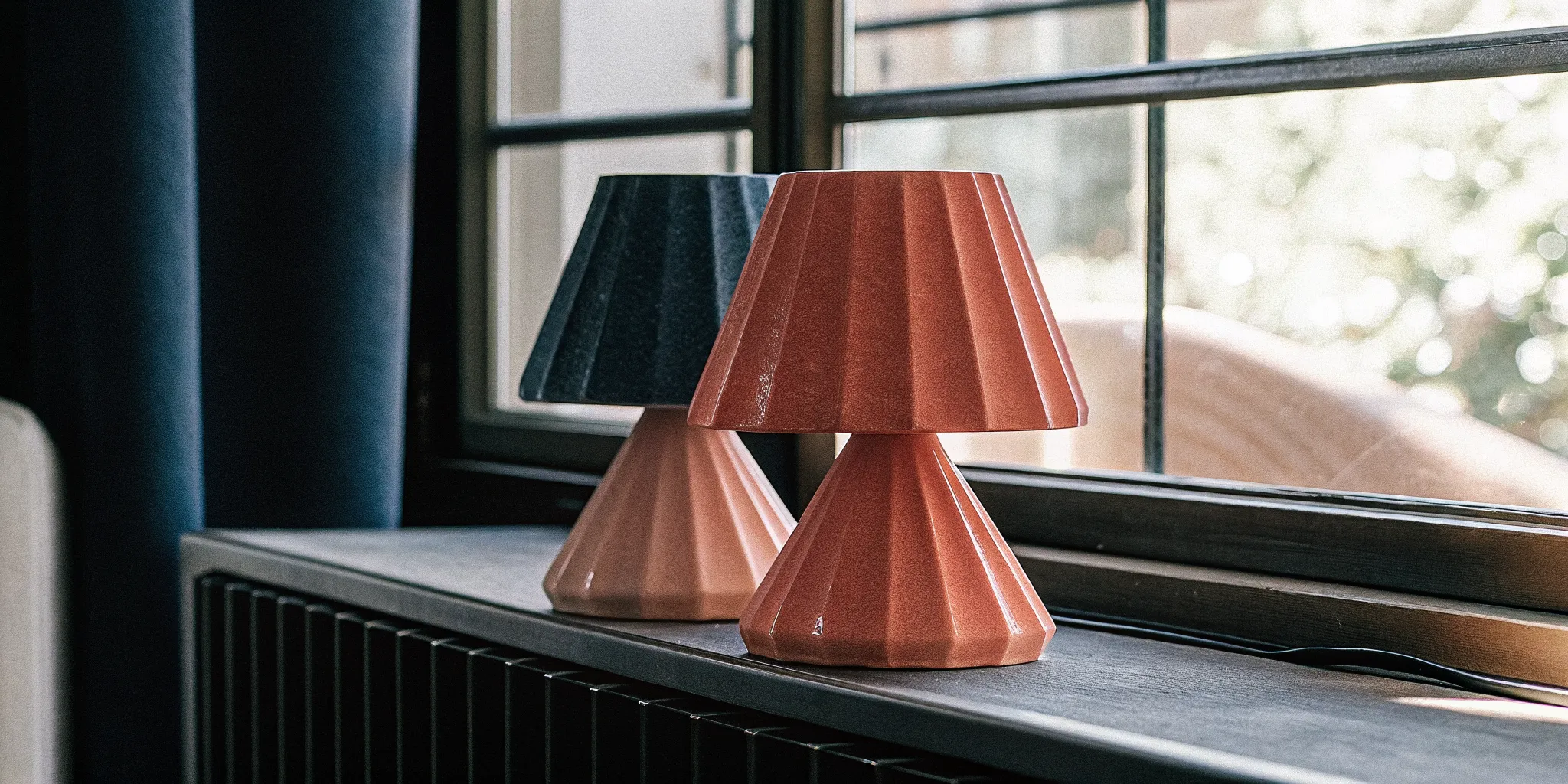 A pair of bold color-blocked steel and ceramic sculptural lamps in blue and peach on a light wall shelf in a calm living room