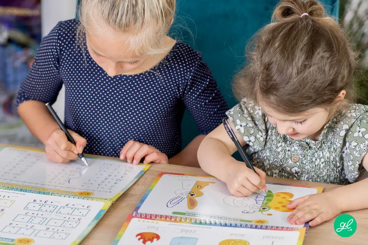 Open cursive workbook on a desk with colorful pencils and eraser nearby