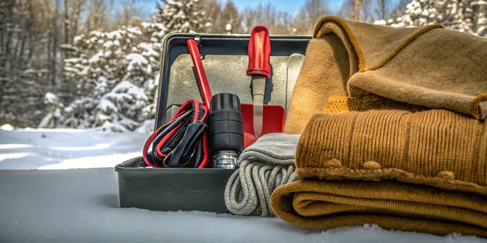 Winter car emergency survival kit with ice scraper, blanket, flashlight, and safety gear arranged on a car seat
