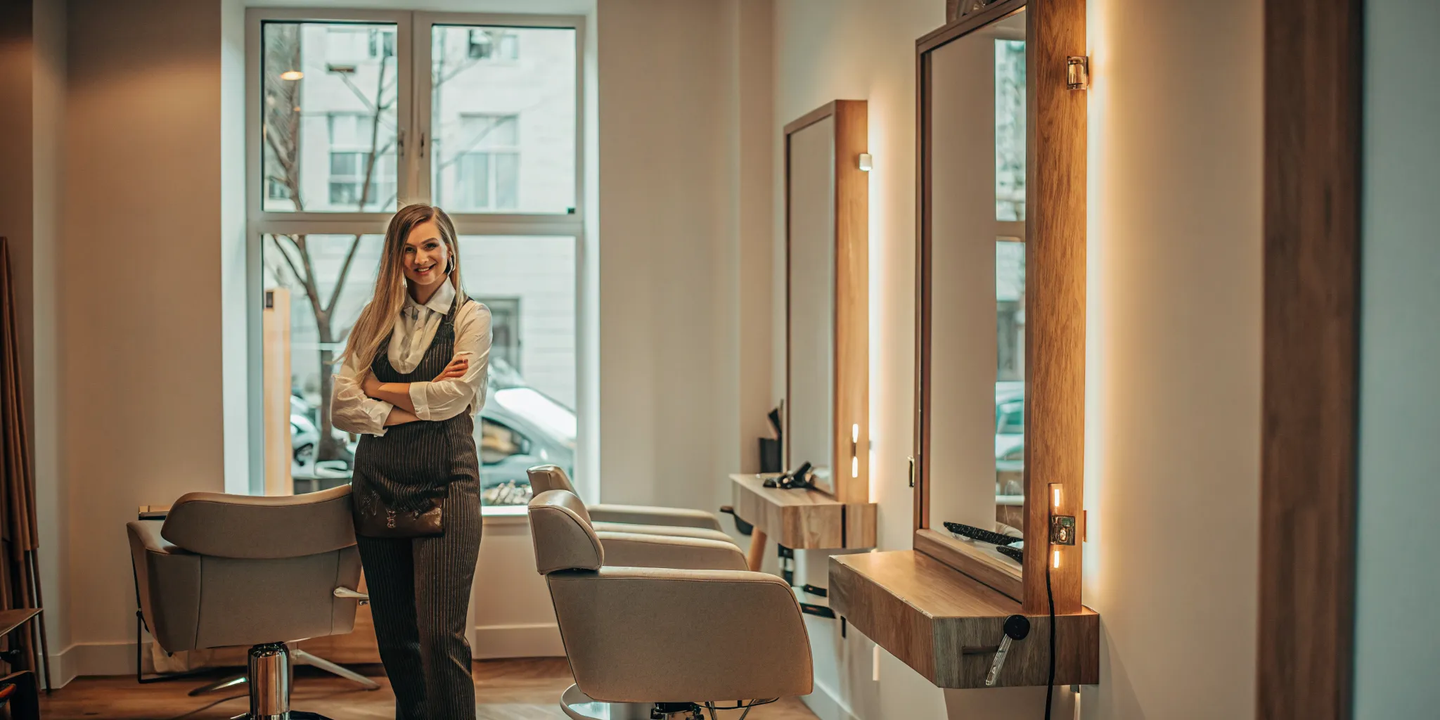 Experienced beauty professional standing confidently inside a private salon suite with professional styling chair and mirror