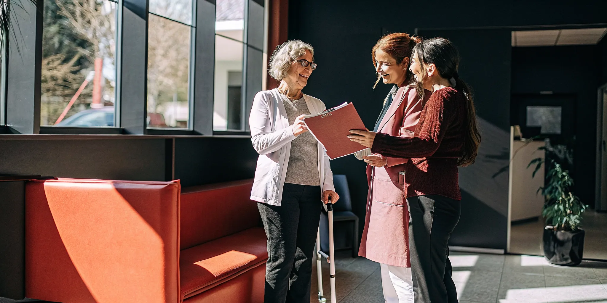 A friendly chiropractor and assistant reviewing a care plan with a relaxed senior woman patient in a bright clinic lobby