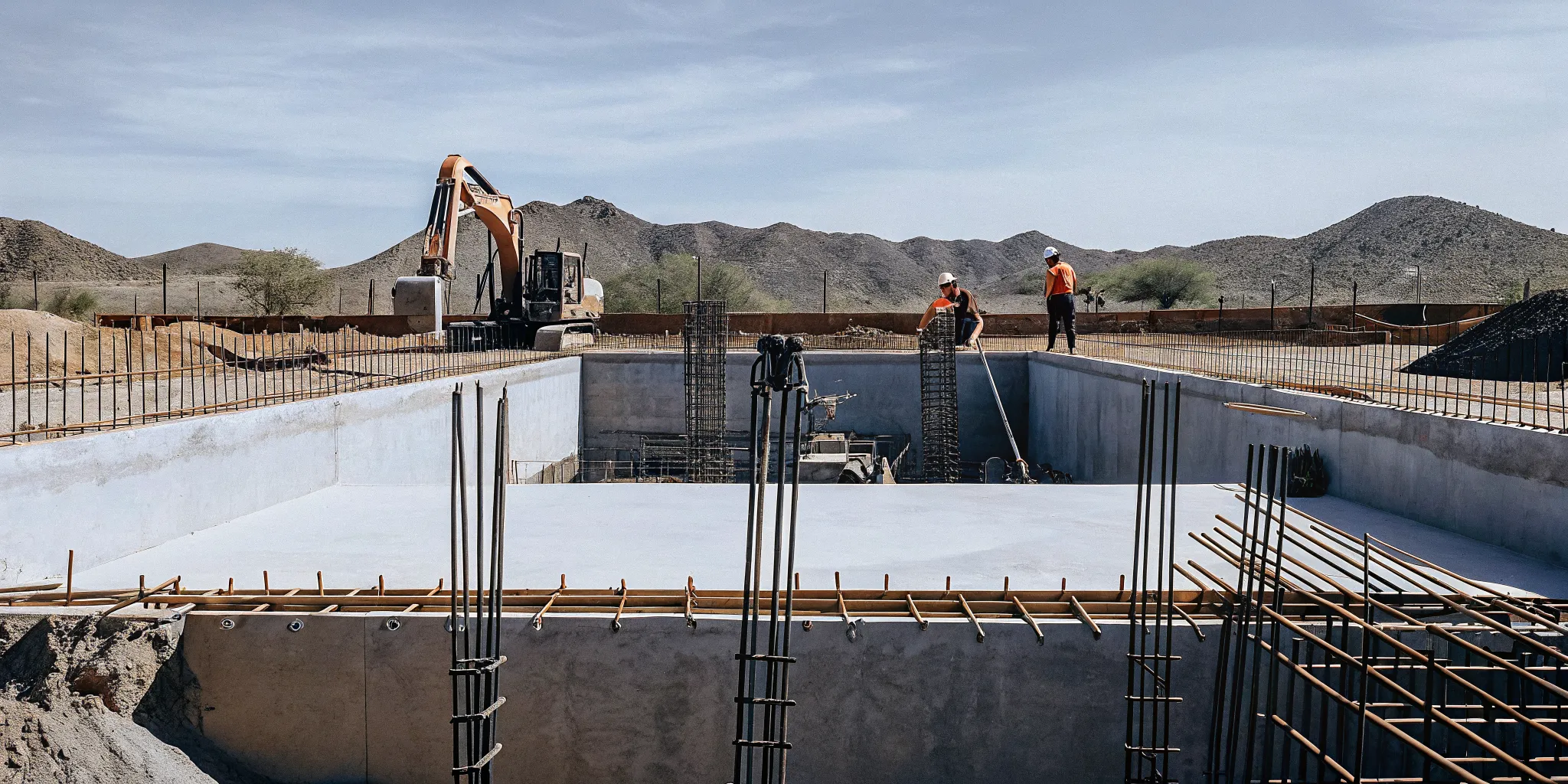 Arizona pool construction site with excavator and steel rebar framework against desert mountain backdrop
