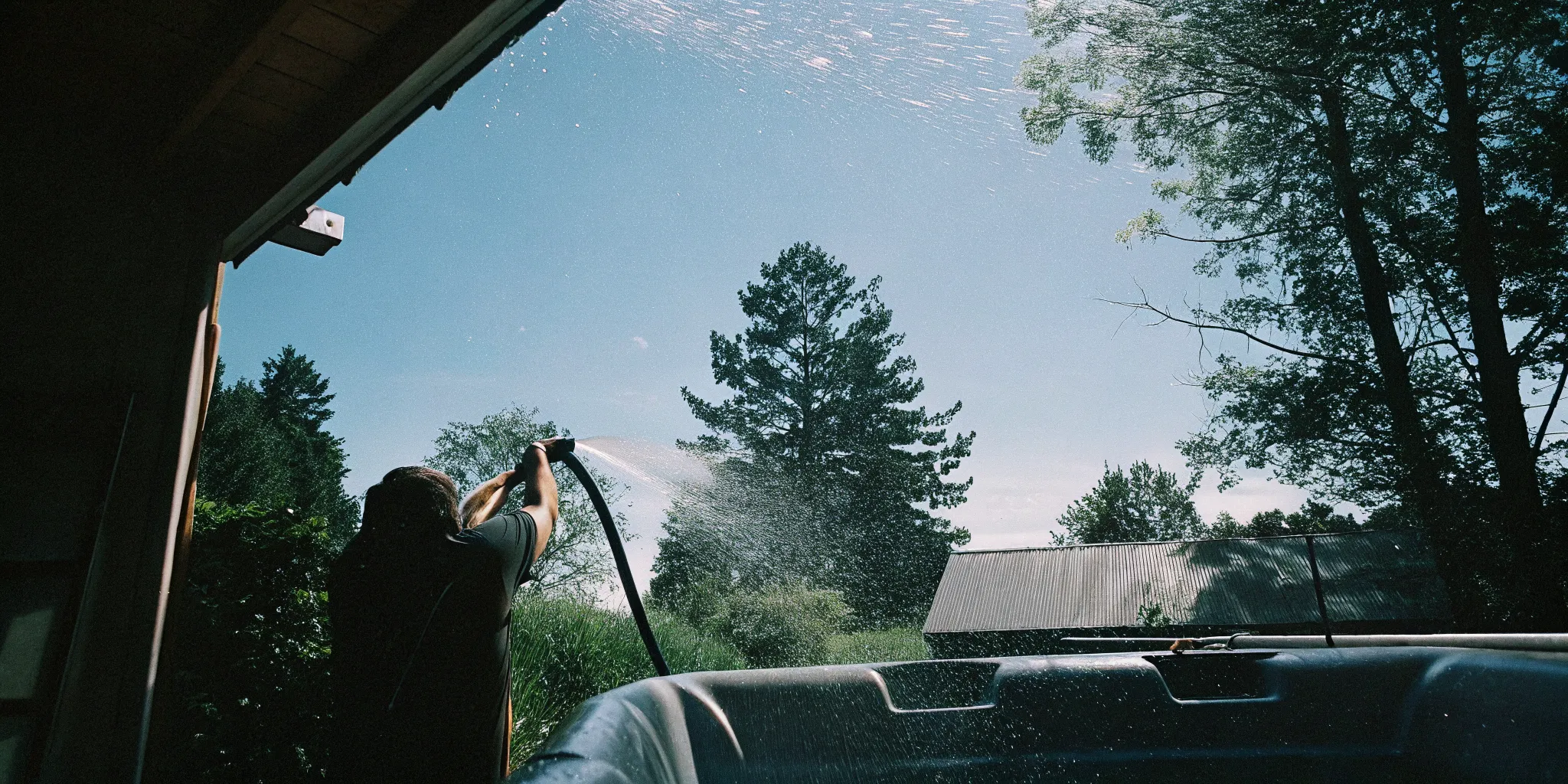 Person rinsing a hot tub filter with a garden hose in a backyard setting