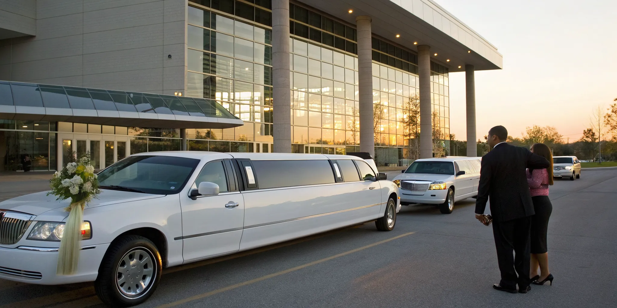 A couple with their white stretch King of Prussia wedding limo at sunset.