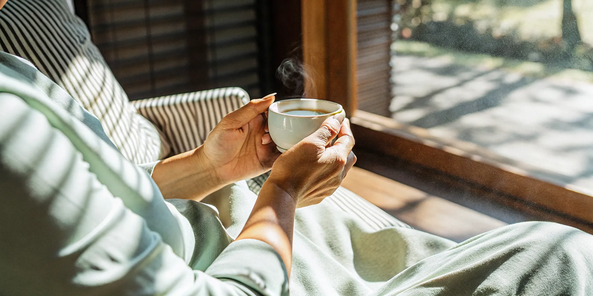 Person holding a warm cup of tea in a calm, sunlit room representing comfort and safety during mental health recovery