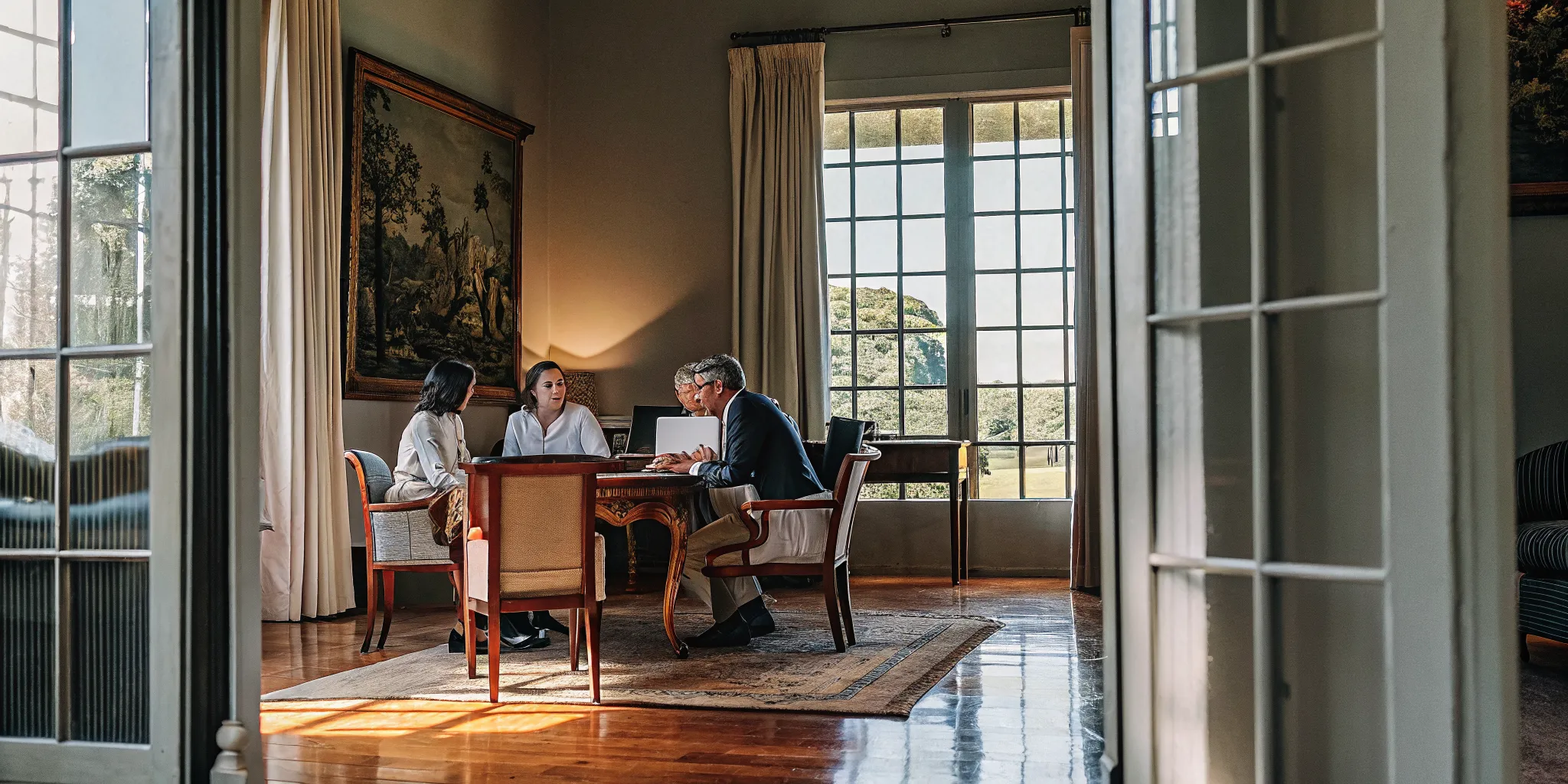 Executive team gathered around a table in an elegant estate meeting room with natural light streaming through tall windows