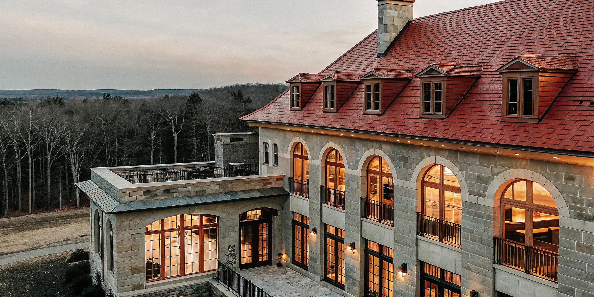 Aerial evening view of a French Chateau private estate in Massachusetts with warmly lit windows and manicured grounds