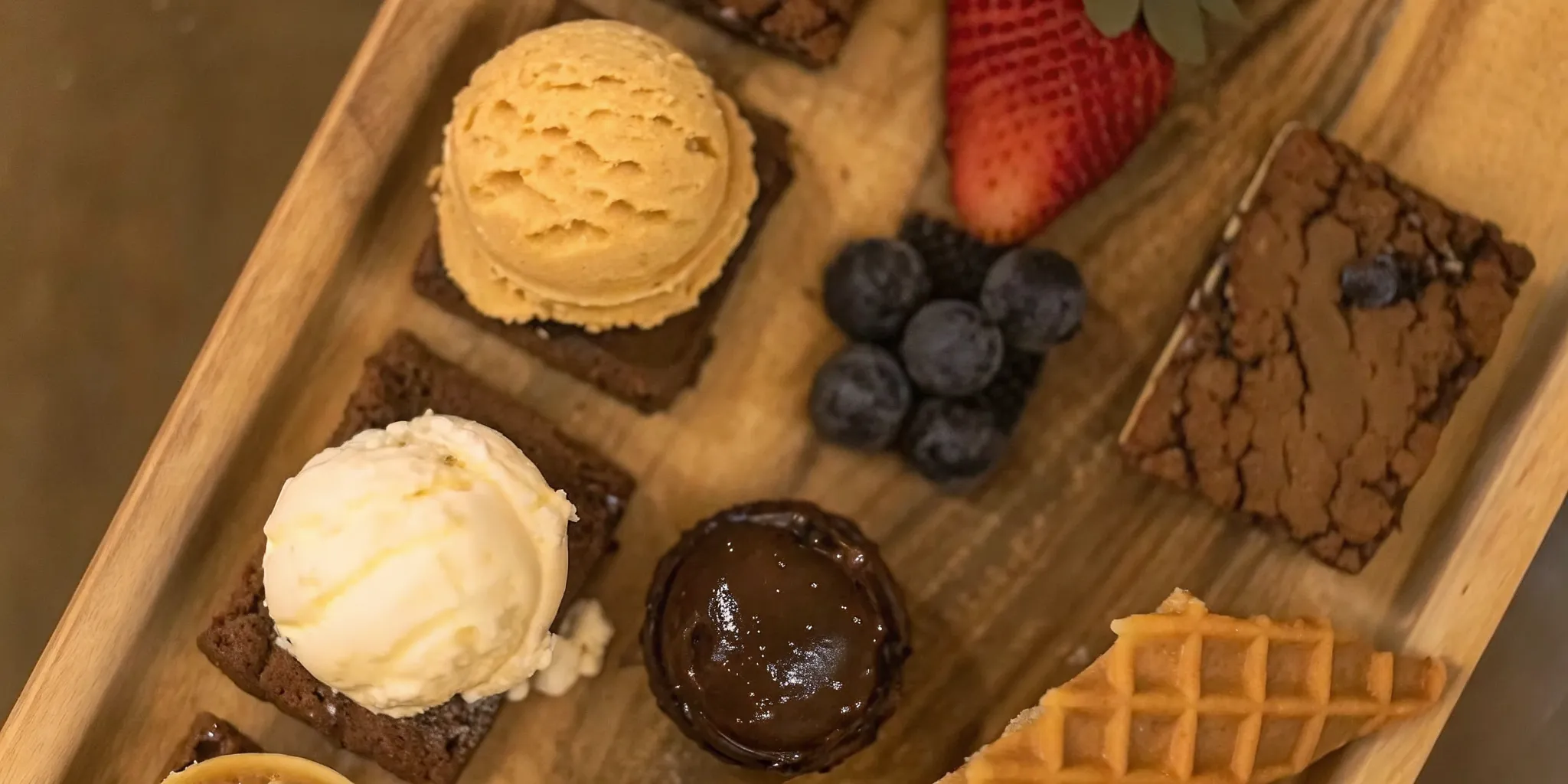 Dessert pairing board with three ice cream flavors, brownies, cookies, berries, and waffle cone pieces on a wooden board