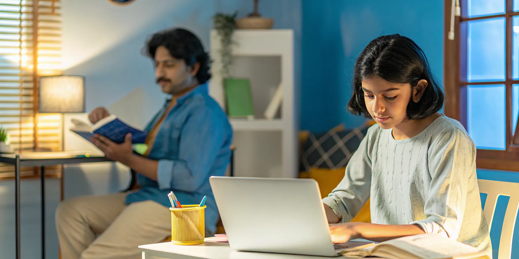 Student studying at a home desk with laptop and learning materials in a bright room