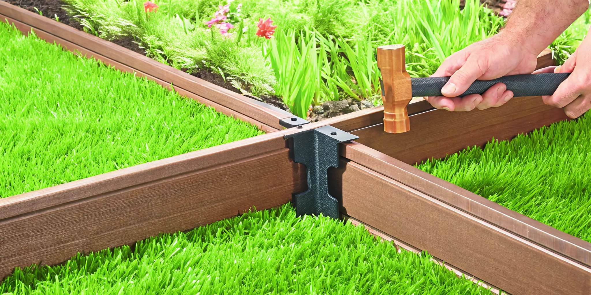 Hands installing composite landscape edging by tapping a Snap-Lock bracket into place with a rubber mallet in a garden setting