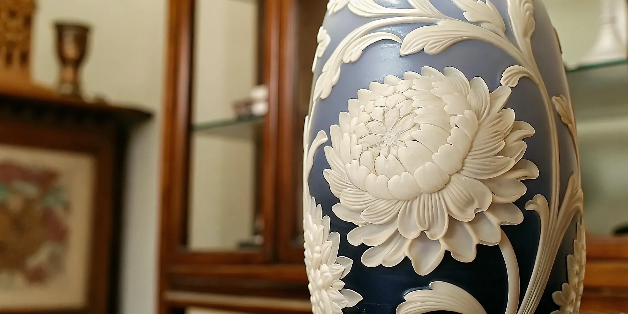 Close-up detail of antique cameo glass carving showing layered white floral relief on dark blue ground