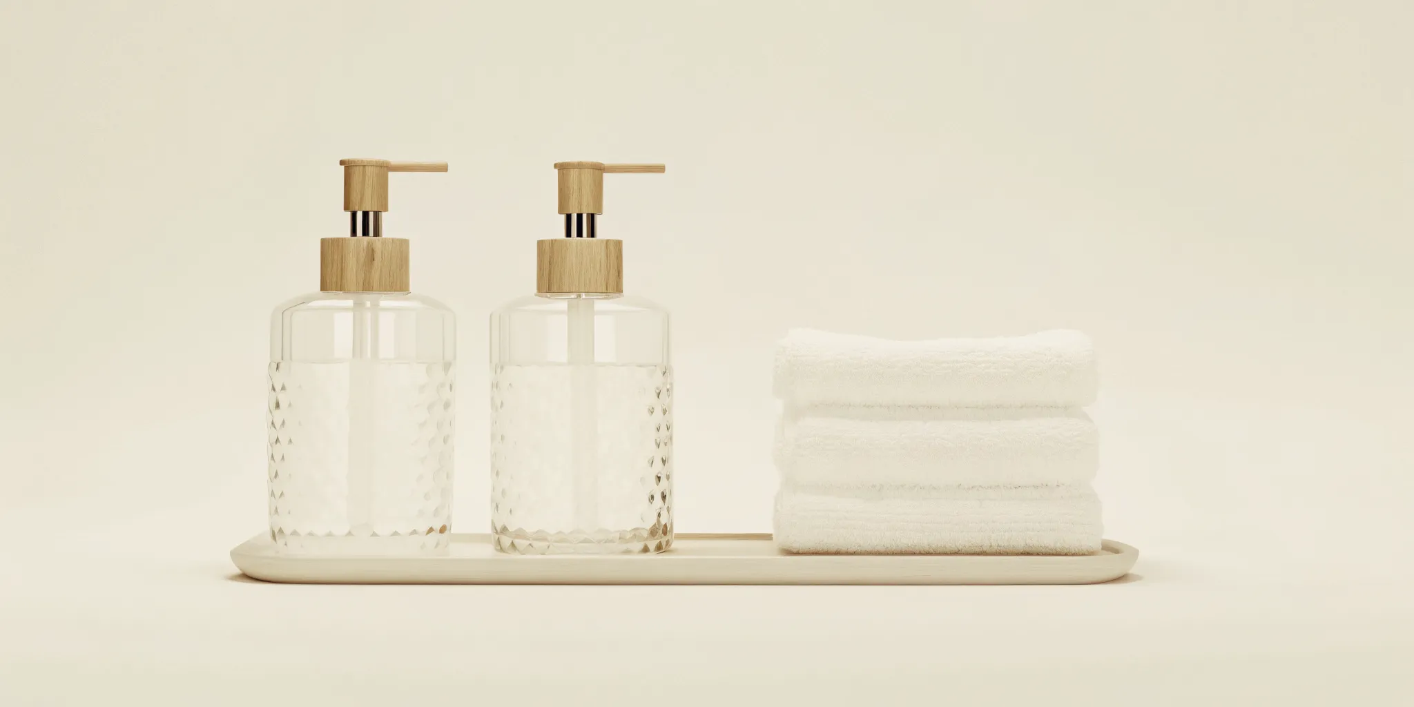 Starter set of refillable glass soap dispensers arranged on a boutique hotel bathroom shelf with folded towels