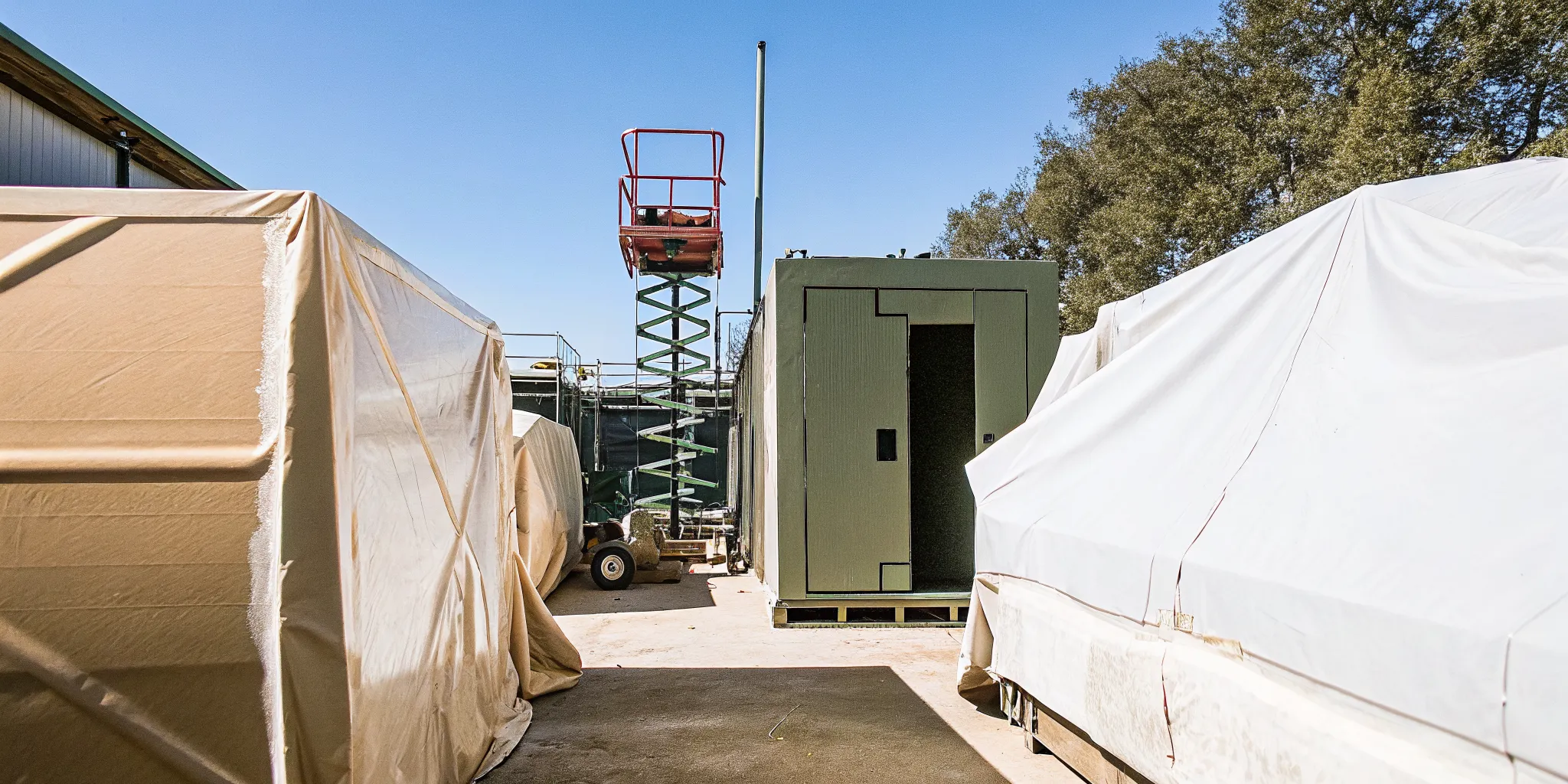 Protected inventory covered in poly sheeting inside a warehouse with scissor lift and masked equipment in the background