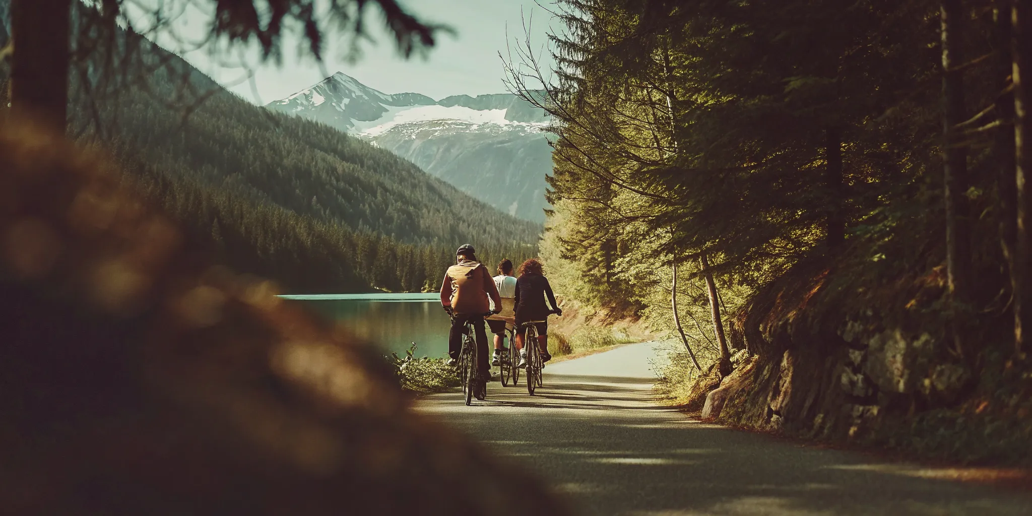 A group of smiling riders on fat-tire electric bikes exploring a scenic paved path next to a clear glacier-fed lake in Whistler