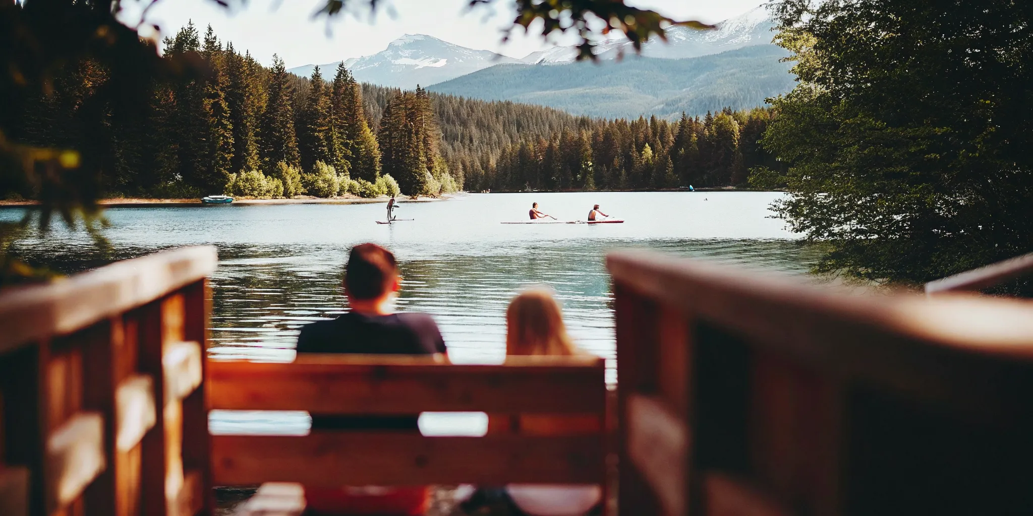 Bright blue Alta Lake in Whistler with people paddleboarding and kayaking on calm water surrounded by green pine forests and mountains