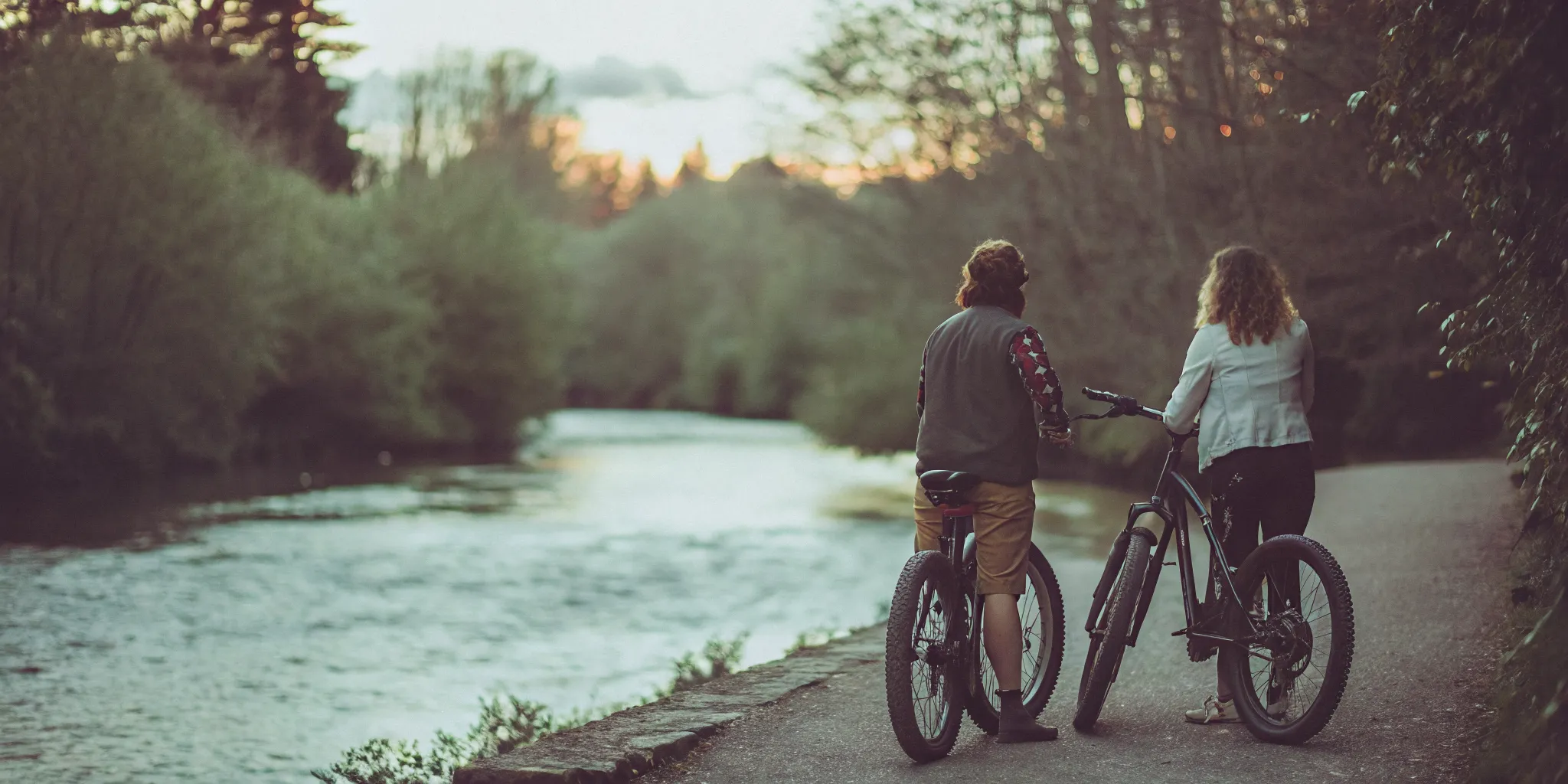 Golden sunset light reflecting off the River of Golden Dreams winding through lush green wetlands and cedar forest in Whistler BC with fat tire eBikes parked on the paved trail