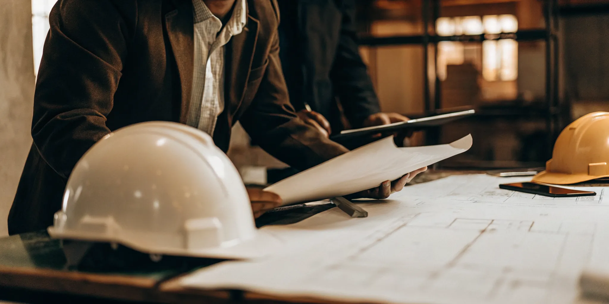 Professional accountant reviewing construction project financial documents at a modern desk with hard hat and blueprints