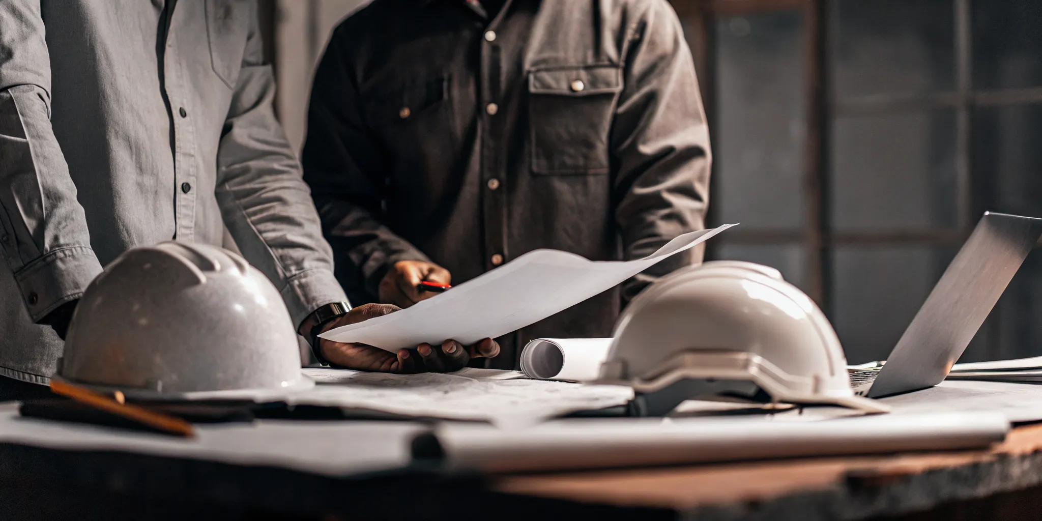 Construction contractor reviewing financial documents and job cost reports at a job site desk with hard hat