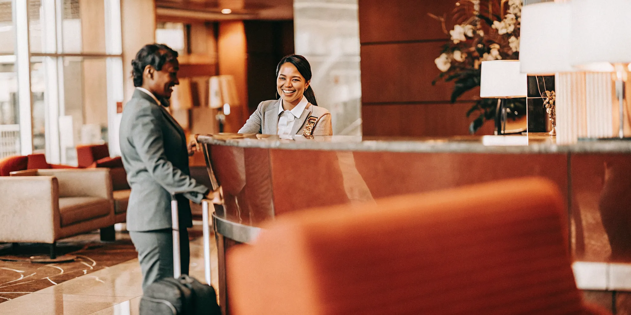 Friendly hotel front desk receptionist smiling and assisting a guest in a luxury hotel lobby