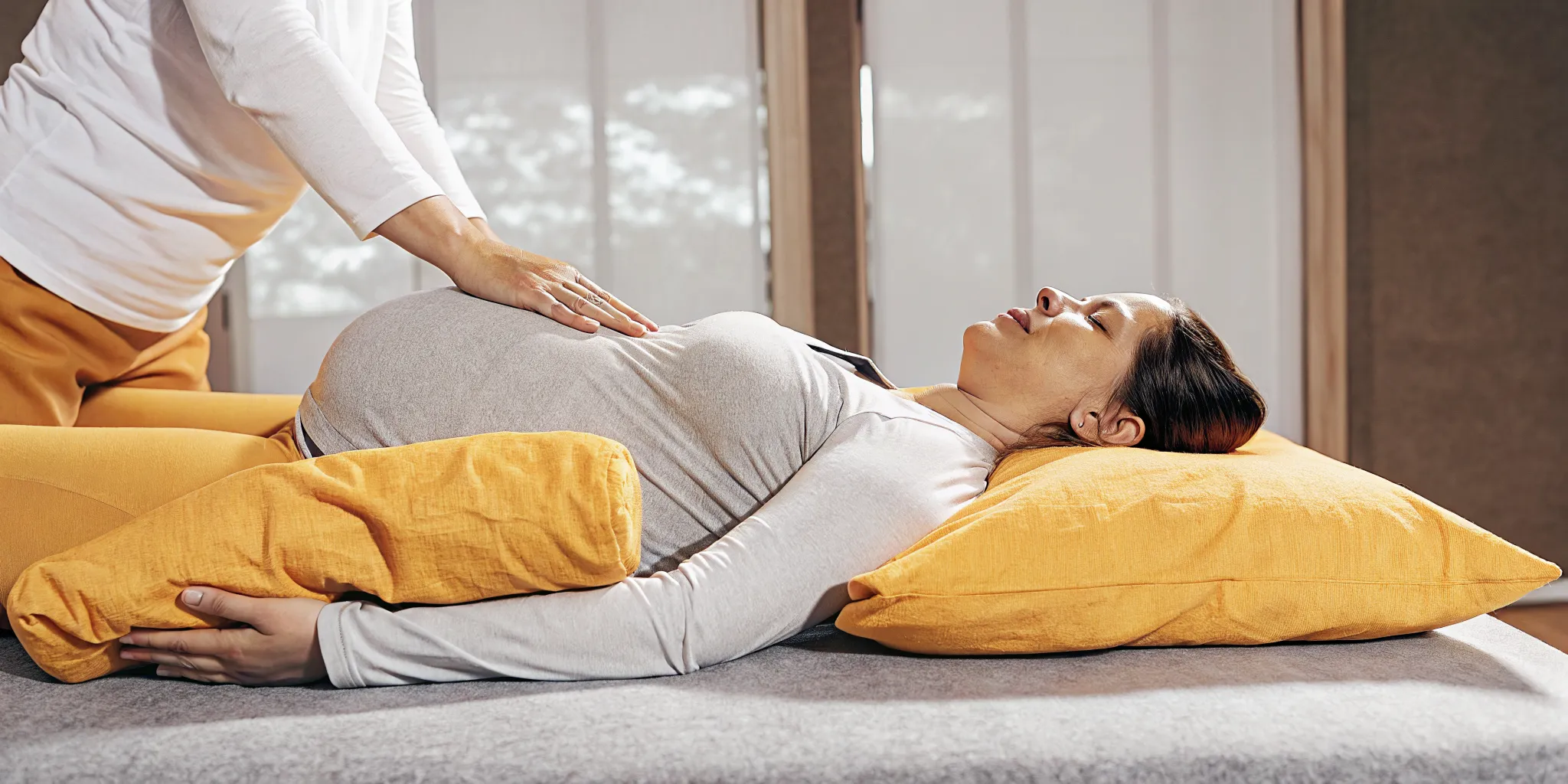 Professional prenatal massage session with therapist applying safe techniques on shoulders while pregnant guest rests in comfortable side-lying position