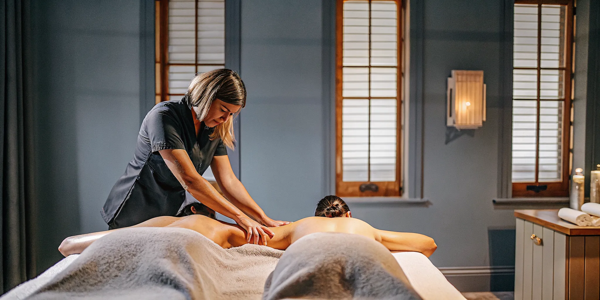 Massage therapist demonstrating long gliding Swedish massage strokes on a guest's back in a warm, professional treatment room