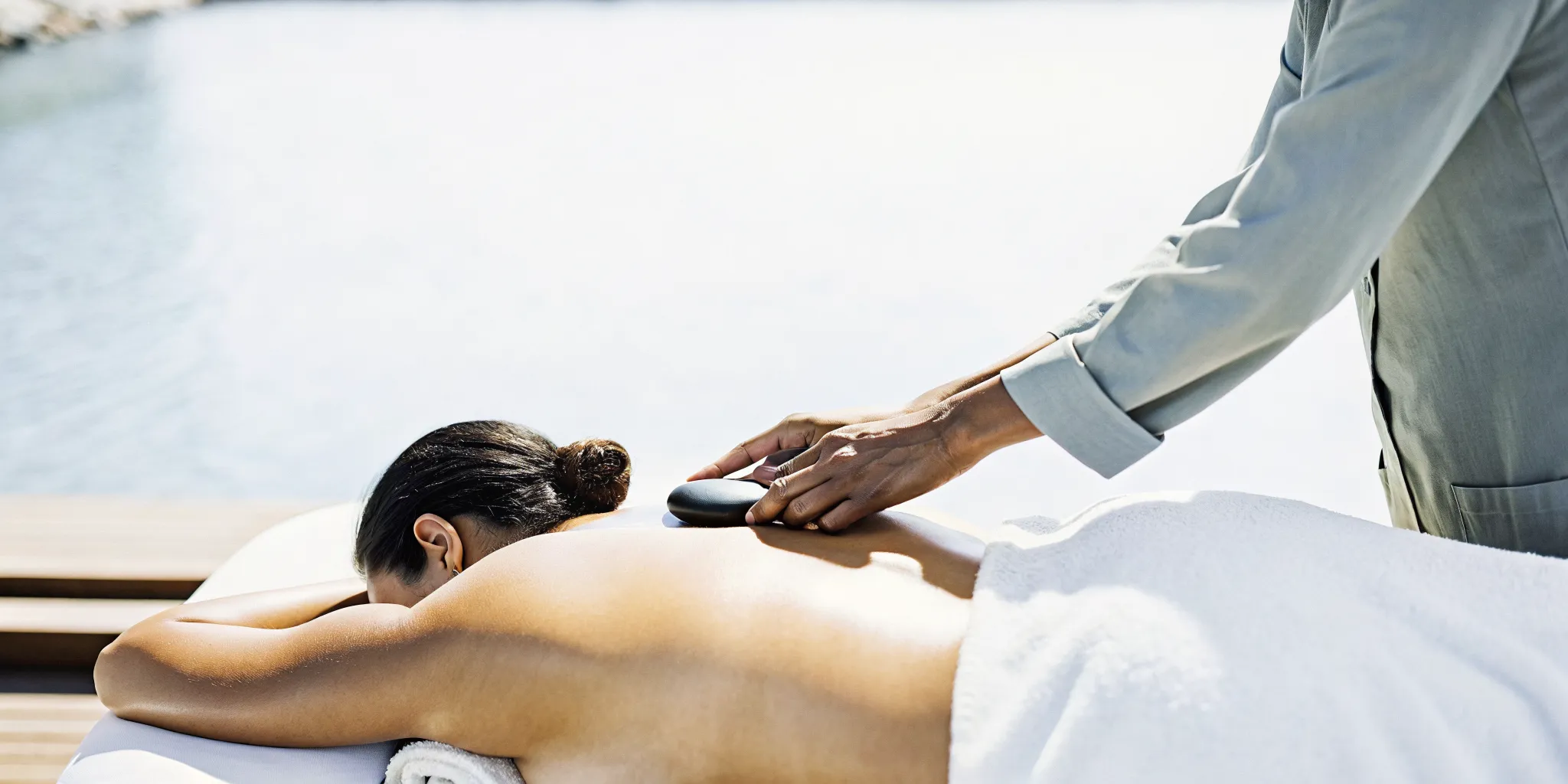 Massage therapist placing a smooth basalt hot stone on a guest's back with a towel barrier