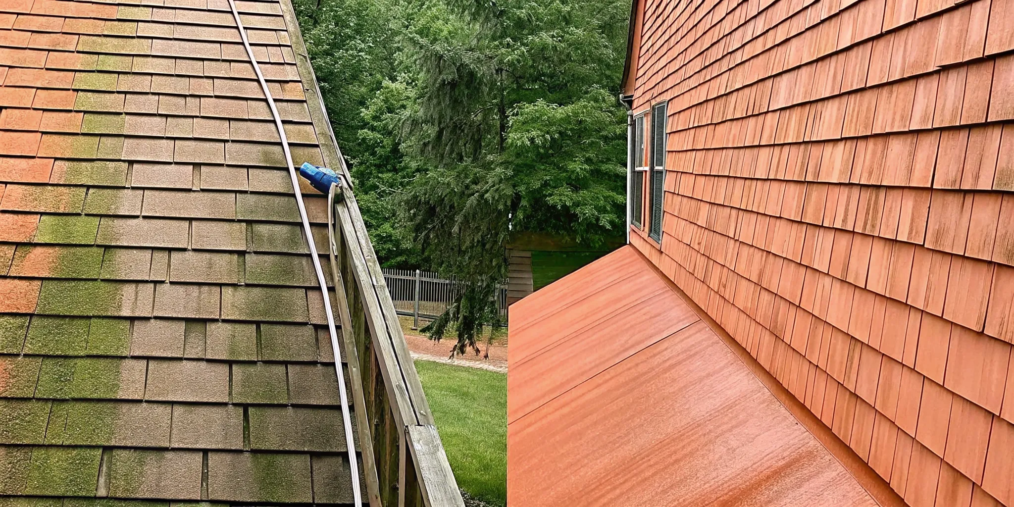 Professional soft washing technician cleaning the side of a luxury cedar-shingle home on Long Island, demonstrating the before and after comparison