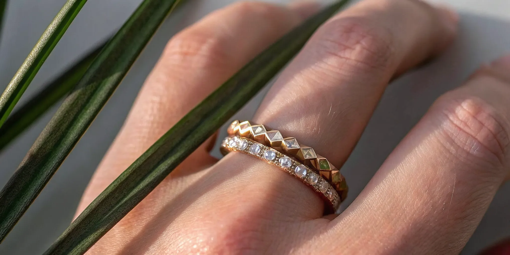 Stacked rings on hand mixing raw diamond, geometric baguette, and smooth gold bands in warm natural light