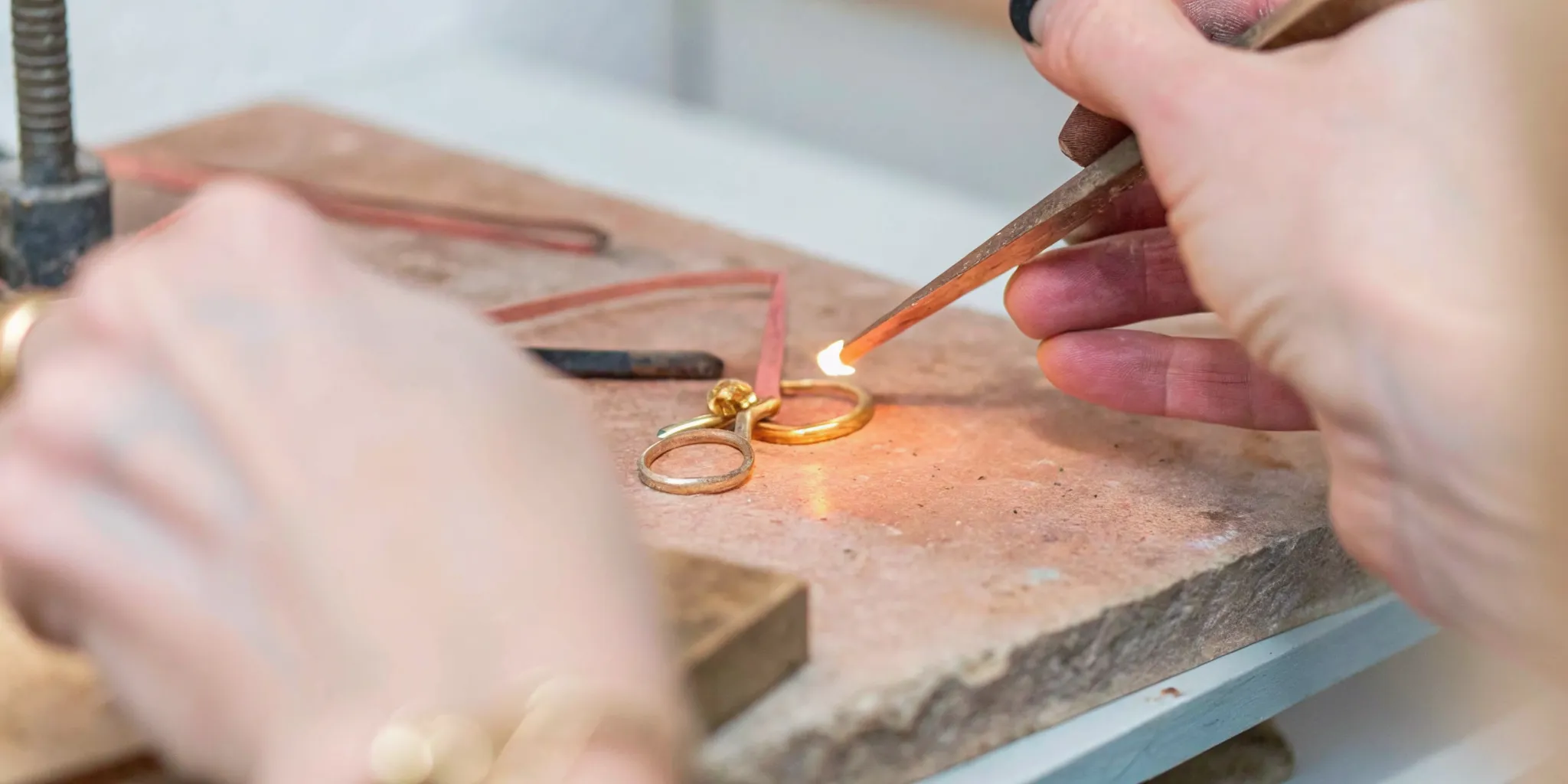 Denver artisan jeweler shaping molten gold at a workbench, traditional handcrafting tools in warm workshop light