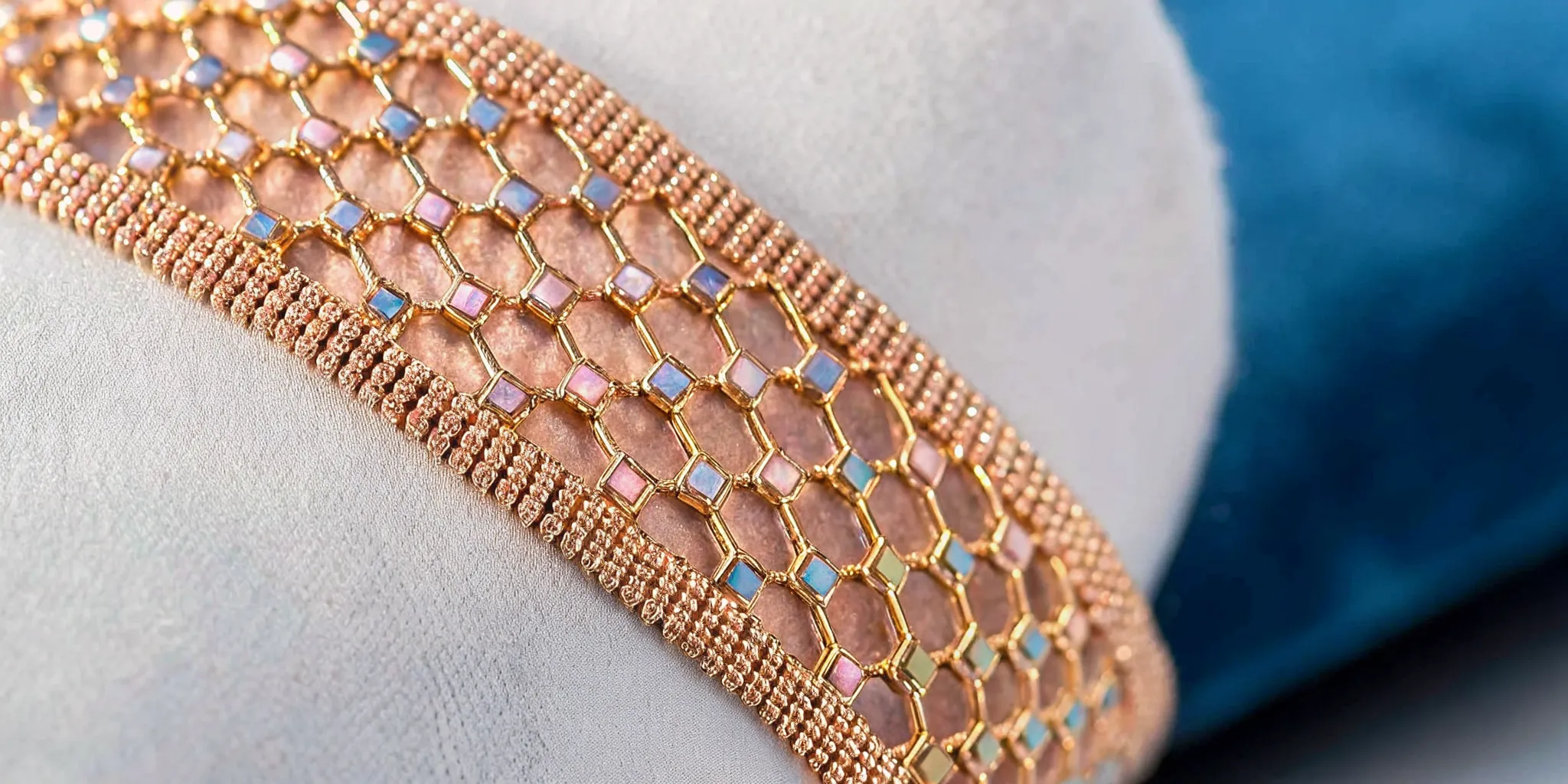 Macro close-up of handwoven 18k gold chain textile jewelry showing intricate weaving pattern around a cabochon gemstone