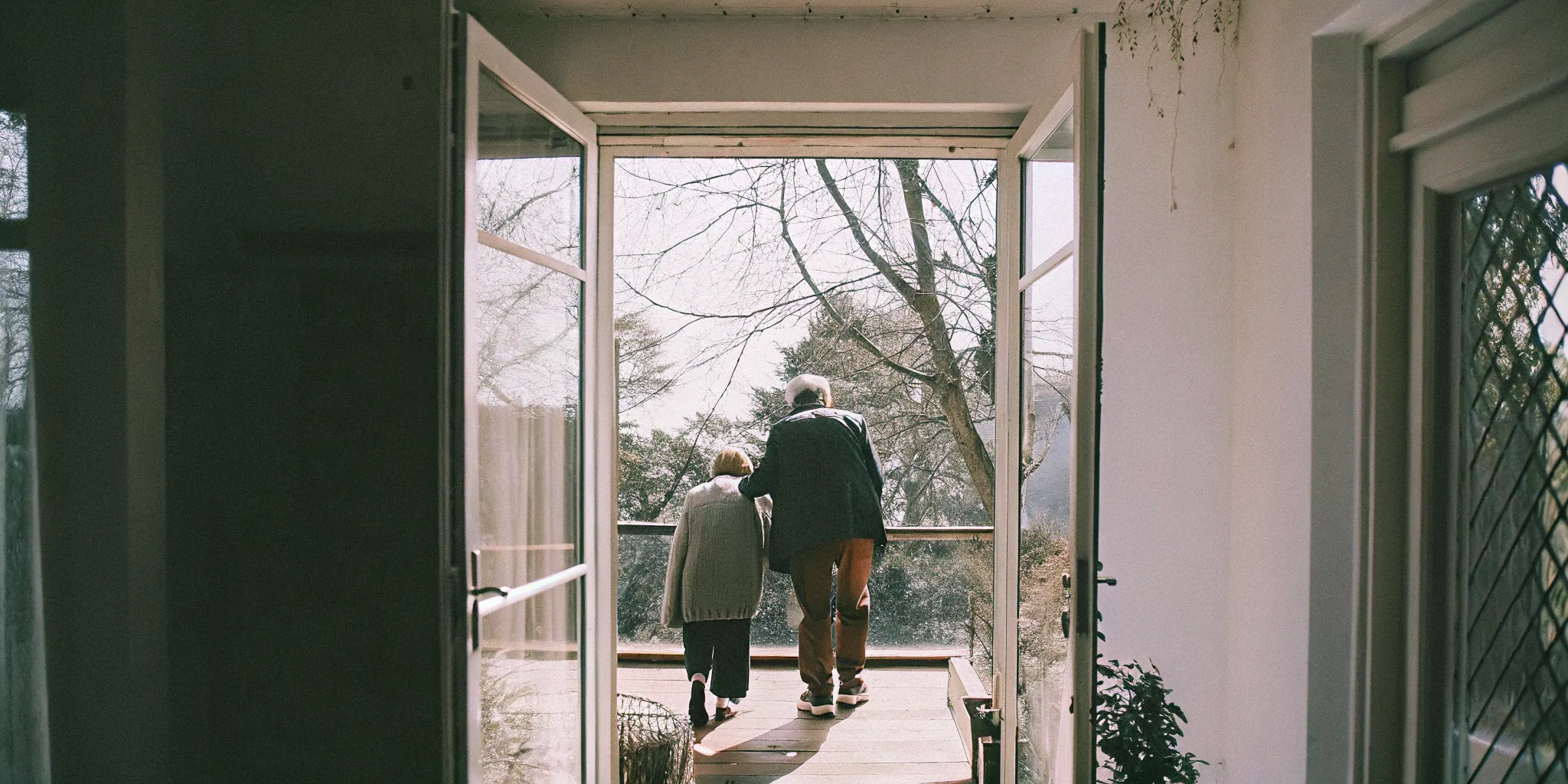 Home caregiver gently steadying an older adult as they walk through a bright, clutter-free living room