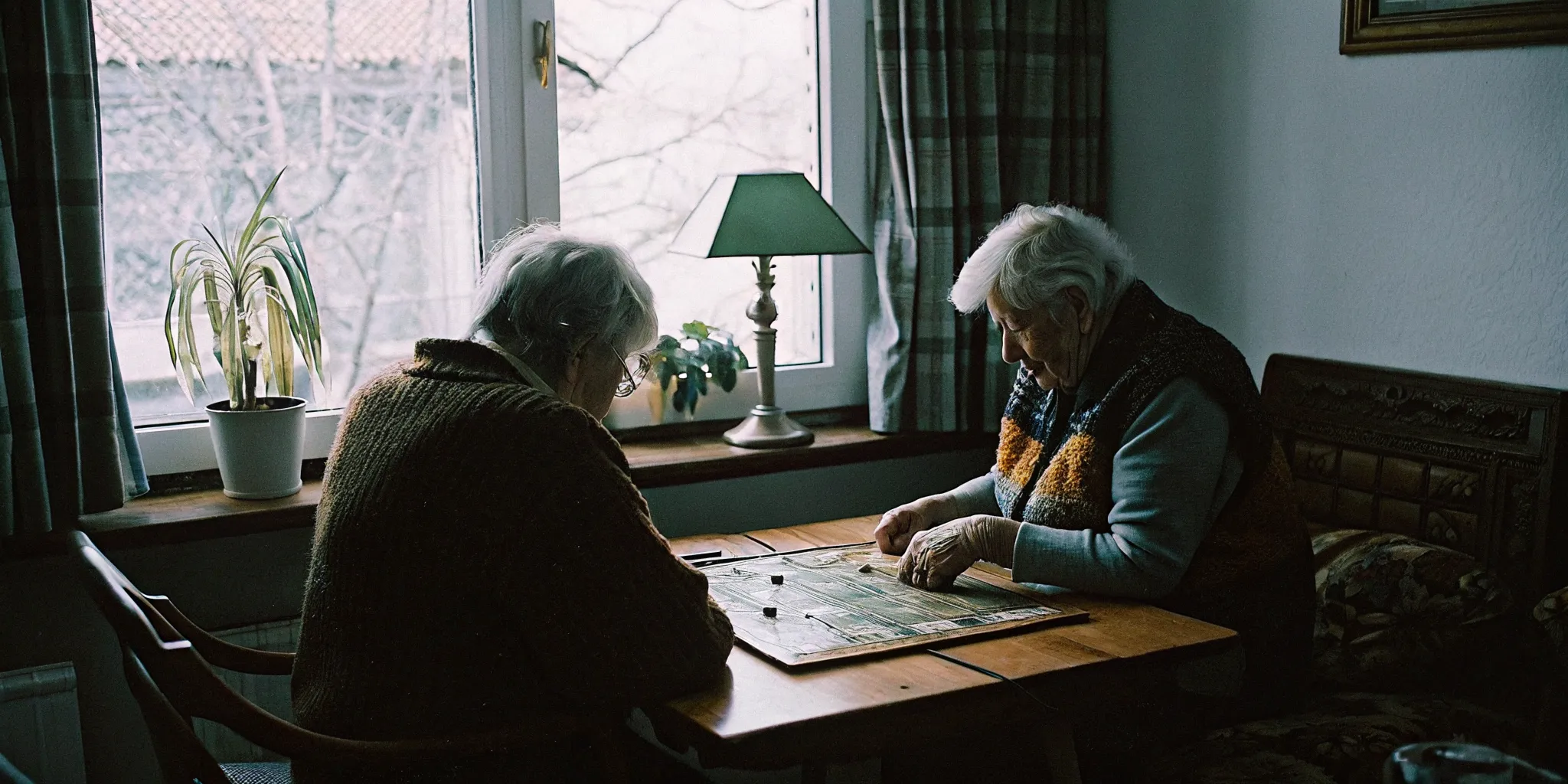 Two seniors playing a board game at a table with a friendly caregiver watching nearby in a warm home setting