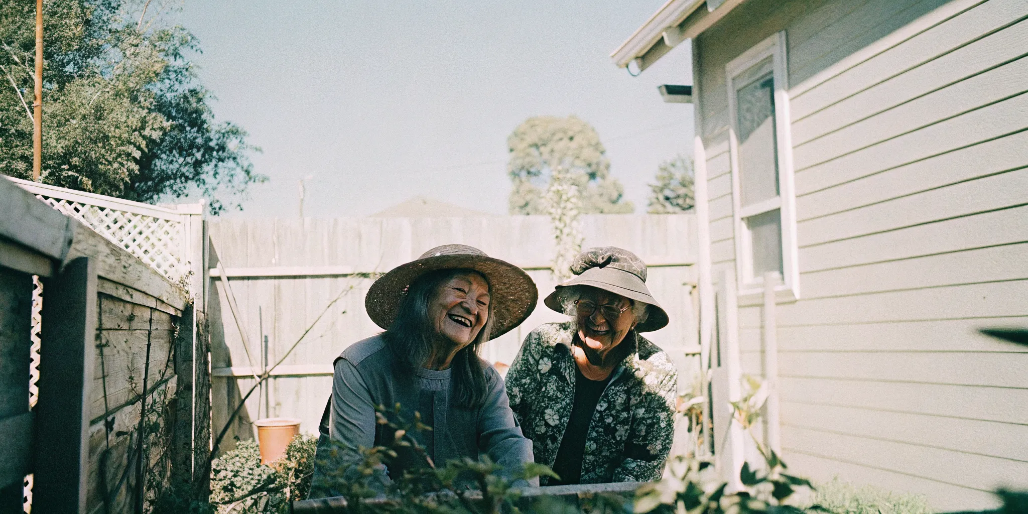 Senior woman gardening in a backyard with a caregiver companion by her side on a bright sunny day