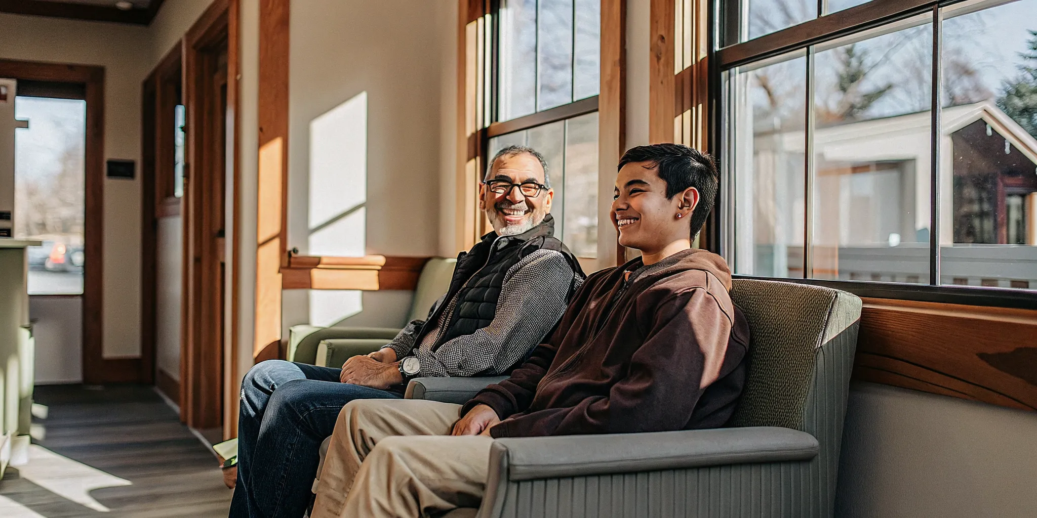 Senior man and teenager relaxing together in the waiting area of a Lowell family dental office