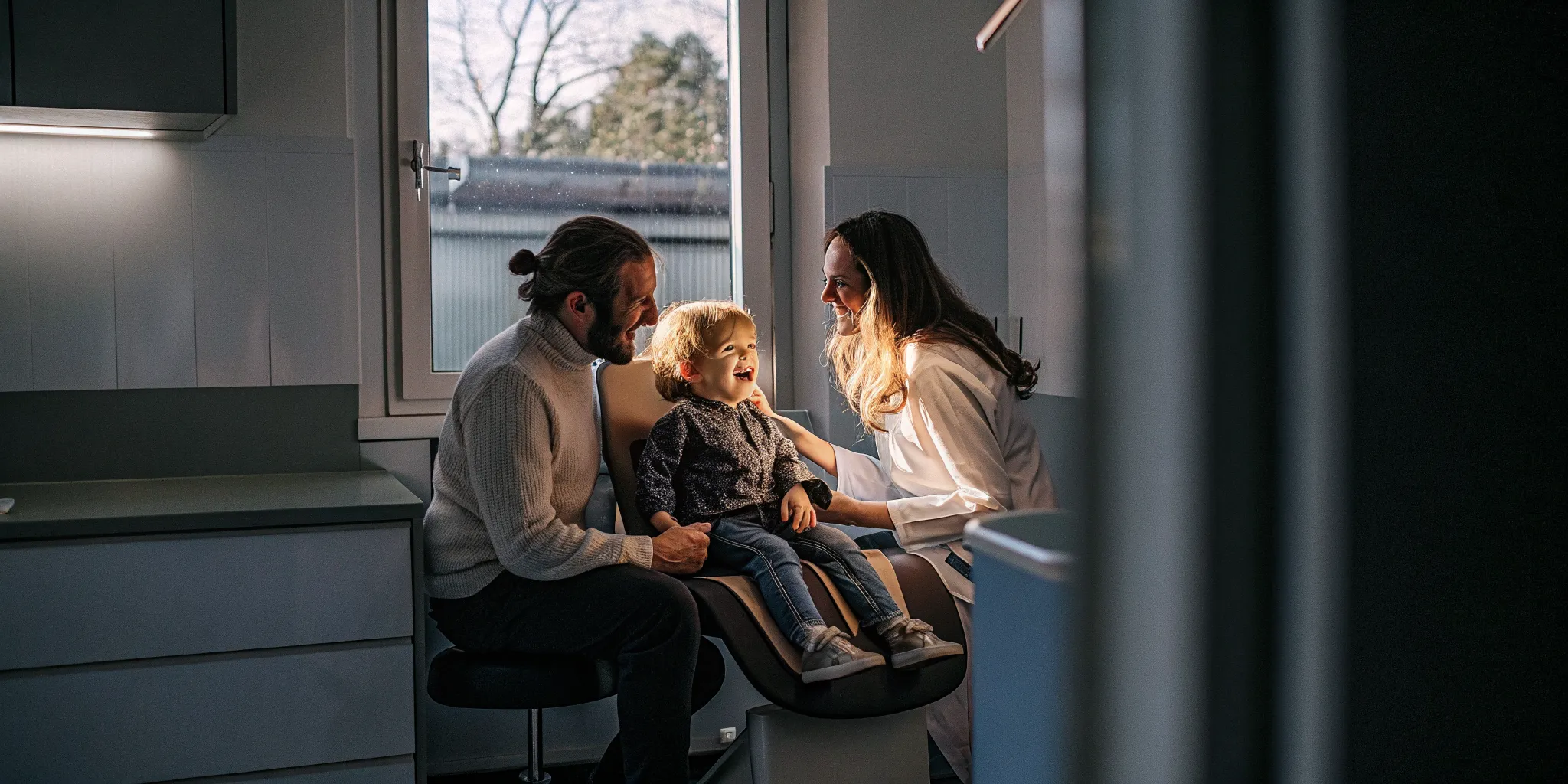 Friendly family dentist welcoming a toddler and parent for a first dental visit in a bright dental office