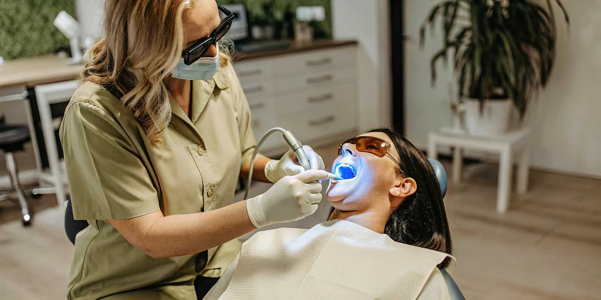 Dental professional performing Zoom teeth whitening treatment with blue LED light activation in a modern dental office