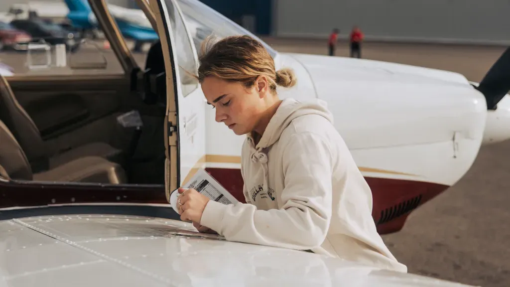 Pilot reviewing a personal minimums checklist beside a small aircraft