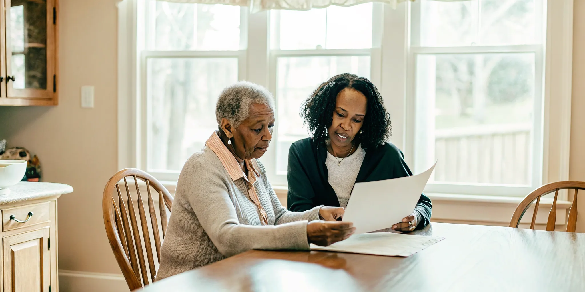 Adult child and senior parent reviewing cost comparison documents at a kitchen table