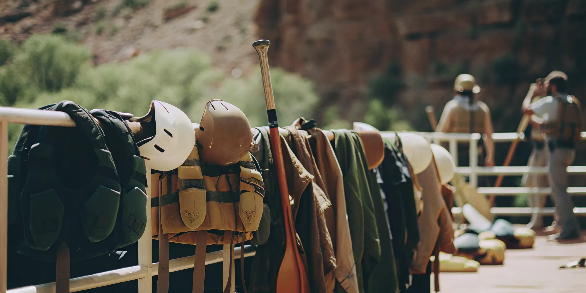 Rafting safety gear including life jackets, helmets, paddles, and dry bags arranged on a dock near the Colorado River