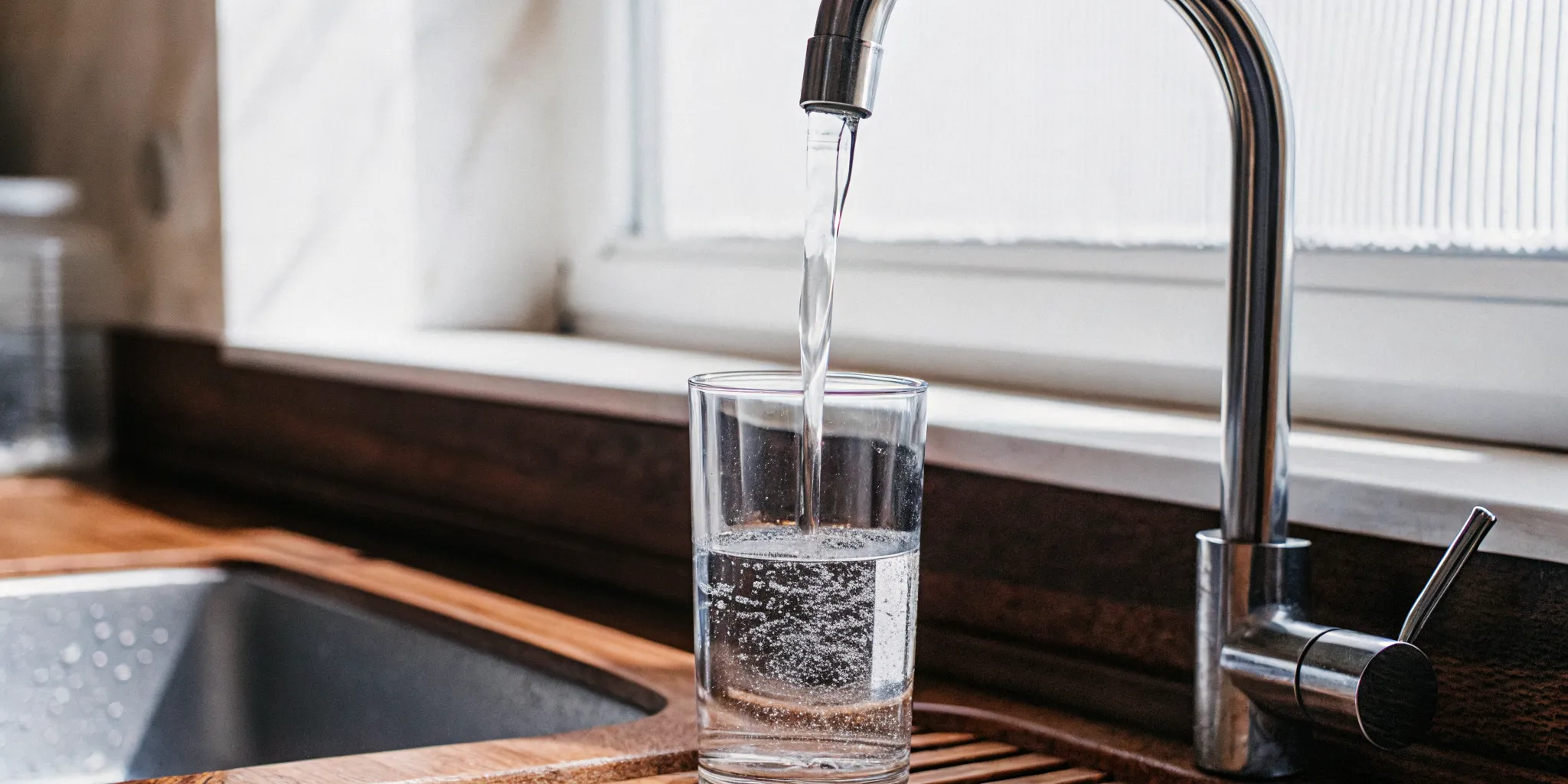 Fresh, clean drinking water pouring from a kitchen faucet into a clear glass